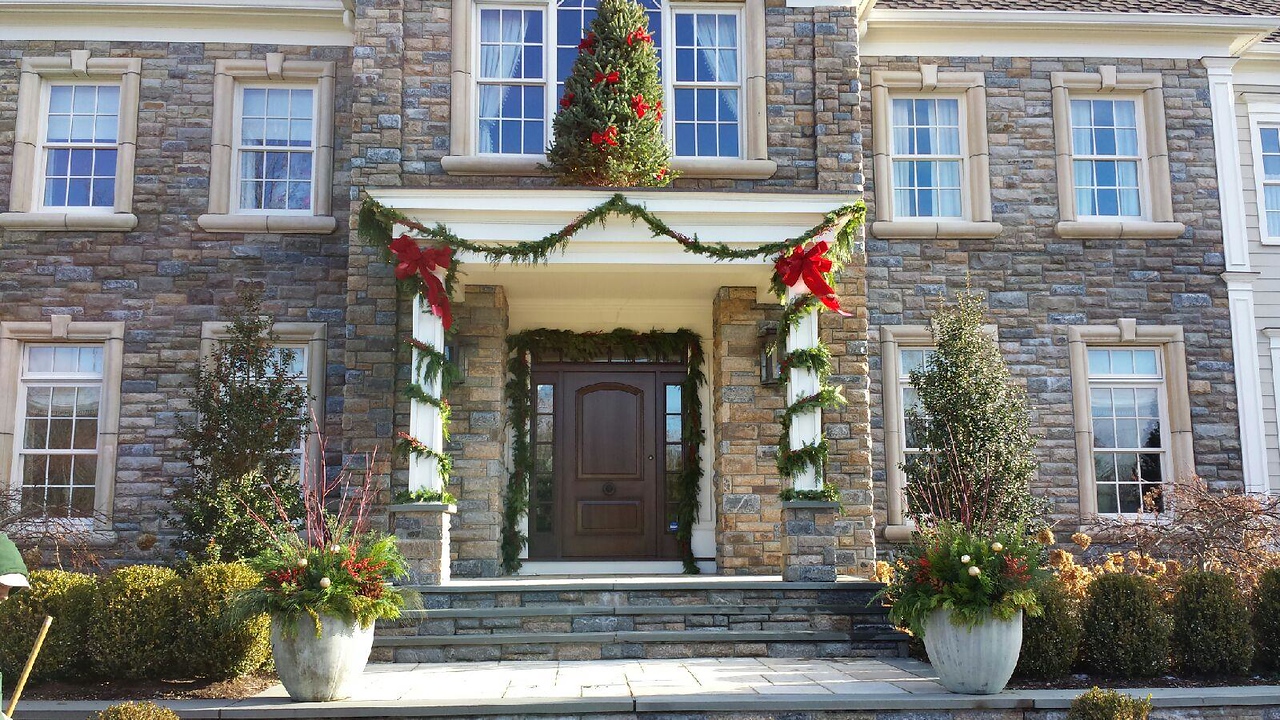 front door frame wrapped in garlands and red ribbon, and surrounded by evergreen trees